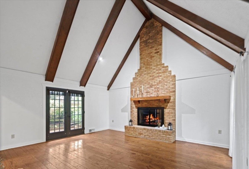 Unfurnished living room with wood-type flooring, beam ceiling, a brick fireplace, french doors, and high vaulted ceiling