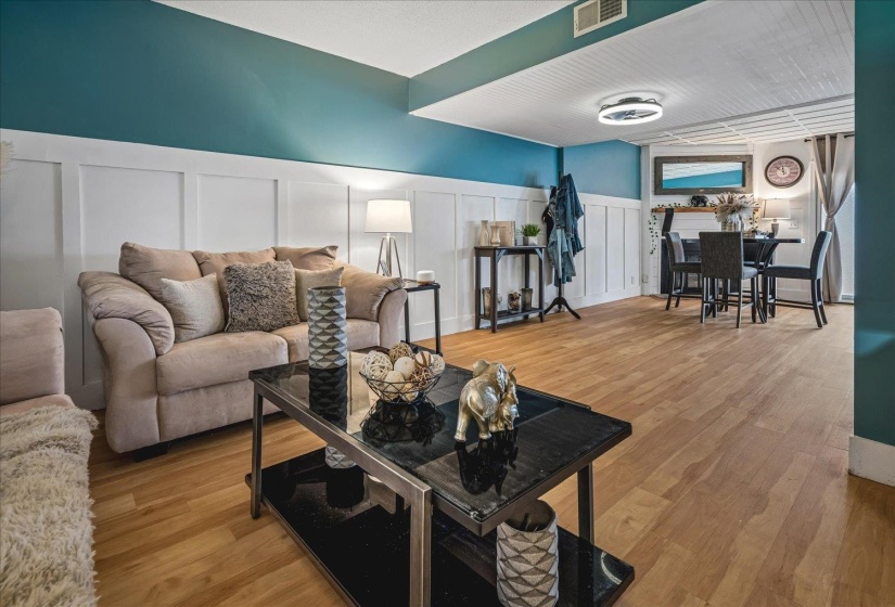 Open-concept living area featuring wood-finish flooring, a contemporary ceiling fixture, wainscoting with a contrasting accent wall, and a built-in mantel