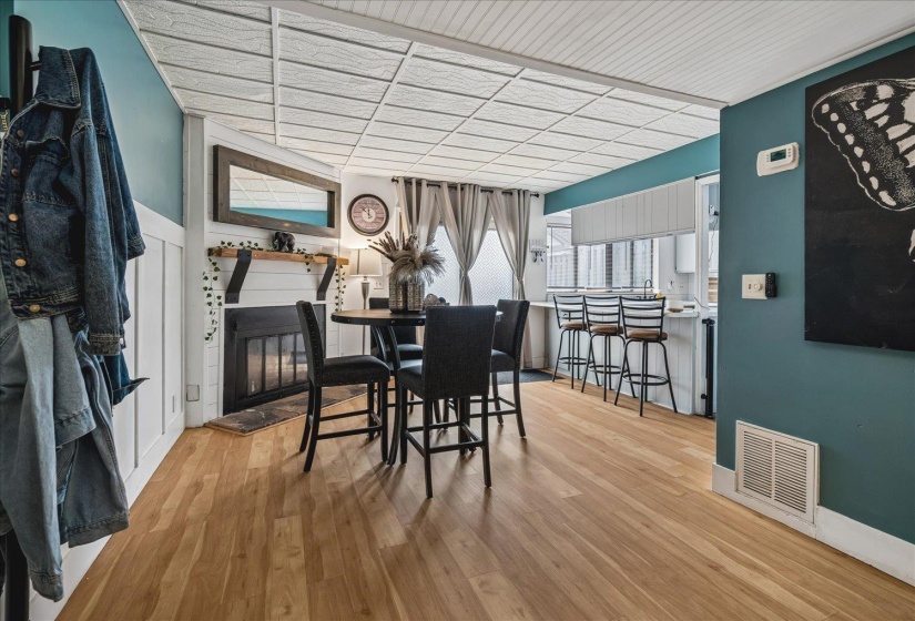 Open-concept living area featuring wood-finish flooring, a fireplace with white shiplap surround, and a kitchen pass-through with bar seating