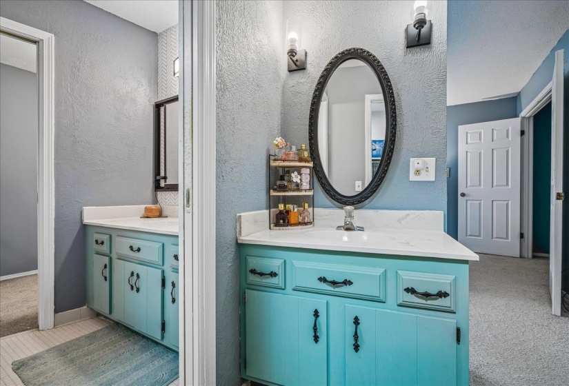 Bathroom vanity featuring teal cabinetry, a white countertop, and a black oval mirror with sconce lighting