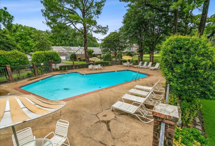 Outdoor swimming pool with a brick coping, surrounded by a concrete patio, and enclosed by a wrought iron fence with brick pillars
