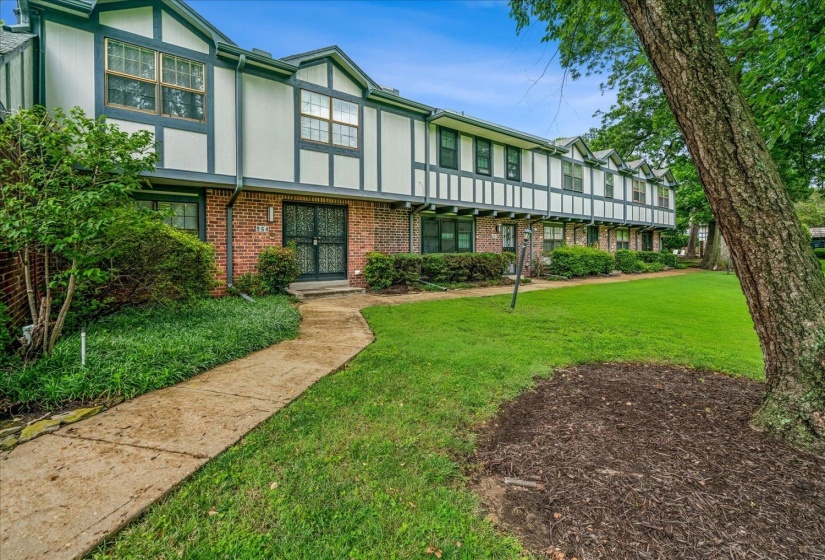 Traditional-style townhome featuring brick and white siding with dark trim, a concrete walkway, mature landscaping, and a manicured lawn