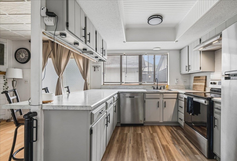 Kitchen featuring light-finish cabinetry, stainless steel appliances, wood-finish flooring, a white countertop, and a built-in breakfast bar