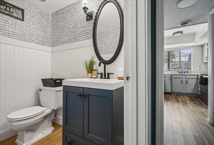 Powder room with a dark blue vanity, white countertop, and black hardware, featuring beadboard paneling and patterned wallpaper
