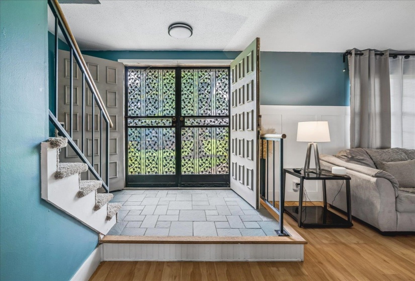 Foyer entry featuring decorative double doors, ceramic tile flooring, and a carpeted staircase with an iron railing