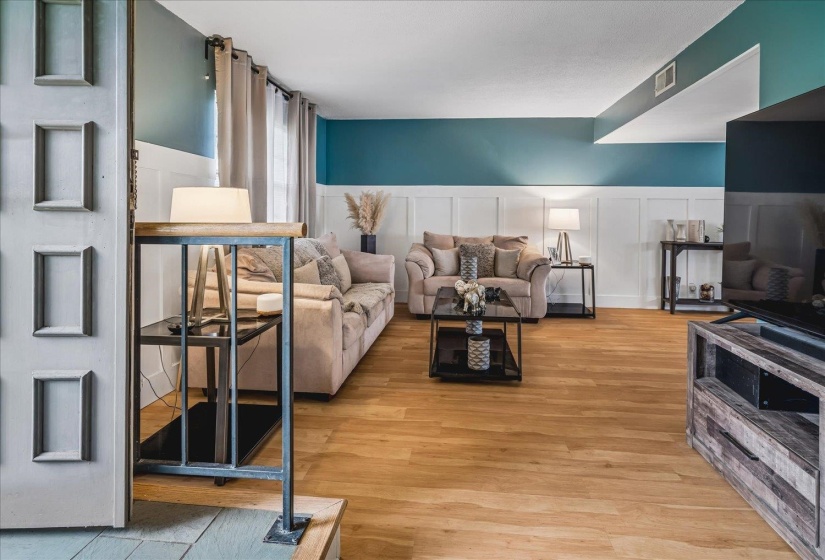 Open-concept living area featuring wood-finish flooring, a contemporary board and batten accent wall, and teal-painted upper walls
