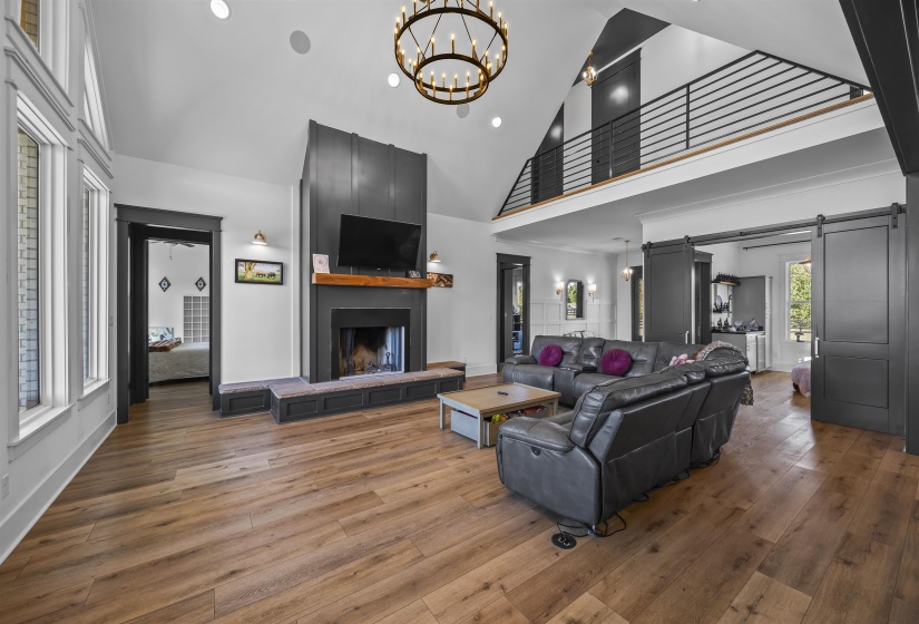 Spacious living area featuring high vaulted ceilings, wood-finish flooring, and a prominent fireplace with a substantial hearth and wood mantel