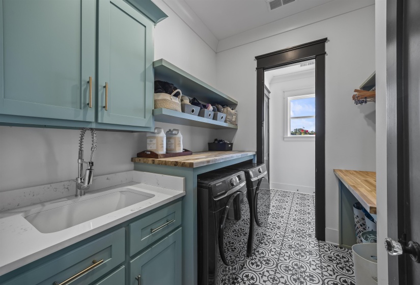 Laundry room featuring patterned tile flooring, teal cabinetry, a white utility sink with a pull-down faucet, and wood-finish countertops