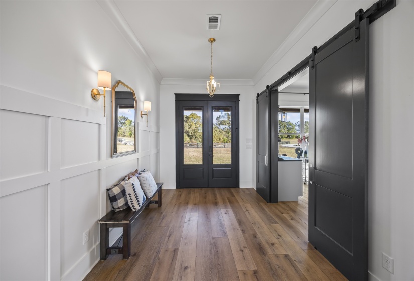 Entryway featuring wide plank wood-finish flooring, white wainscoting, and a pair of dark-paneled double doors