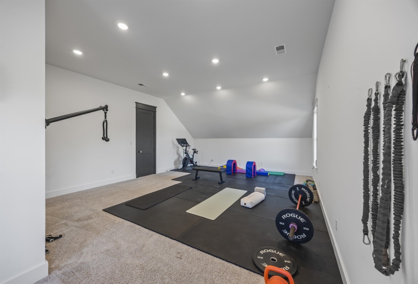 Spacious room featuring sloped ceilings, recessed lighting, and mixed flooring with carpet and rubber mats