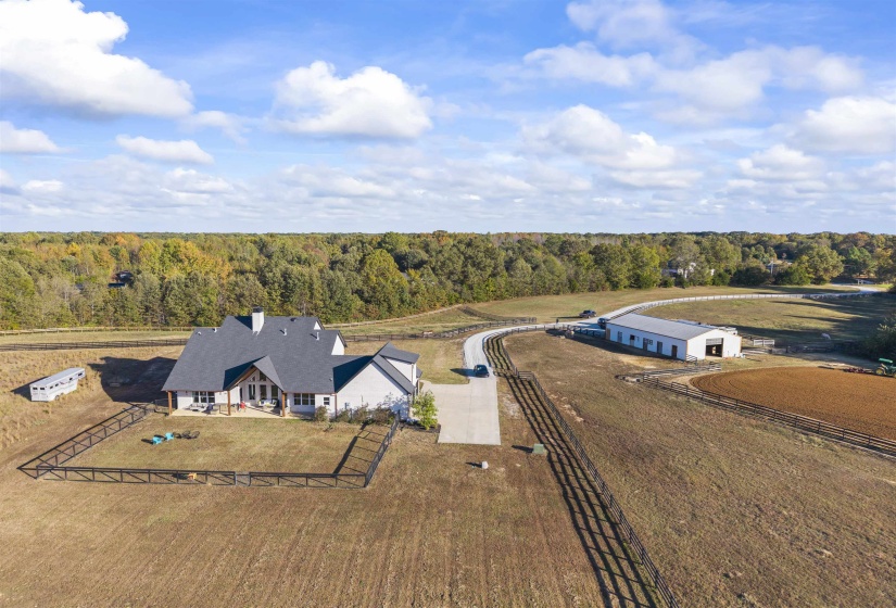 Expansive property featuring a contemporary residence, a large outbuilding, a fenced riding arena, a concrete driveway, and extensive perimeter fencing