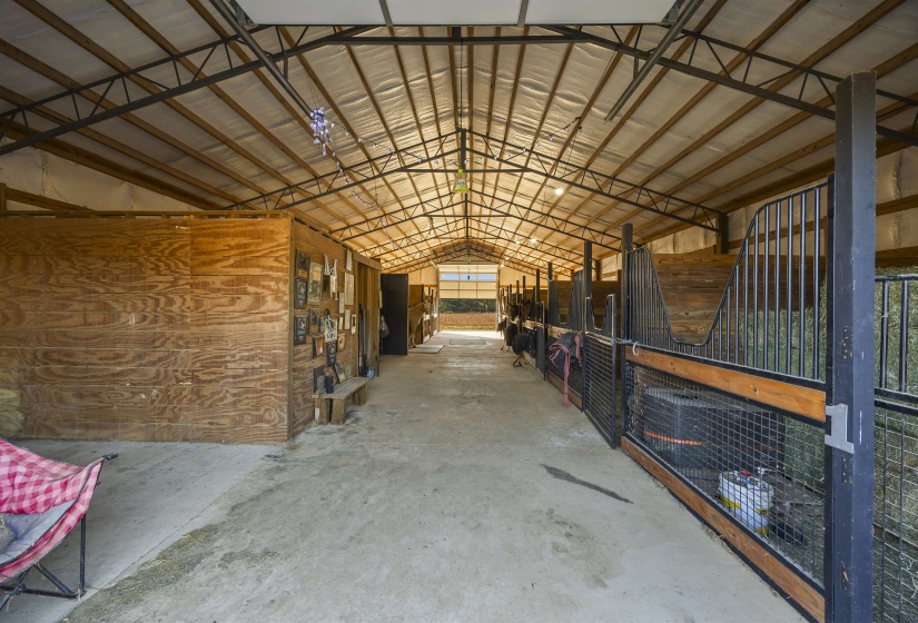 Spacious barn interior featuring an exposed metal truss roof system, concrete flooring, and multiple stalls with black metal gates and wood accents