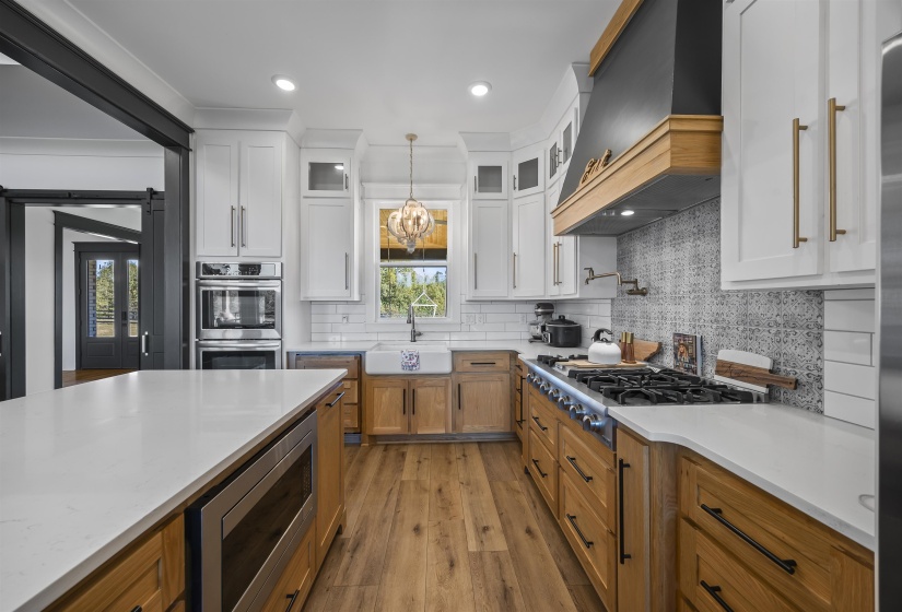 Gourmet kitchen featuring a large island with white stone countertop, built-in microwave, white upper cabinetry, natural wood-finish lower cabinetry, and wood-finish flooring