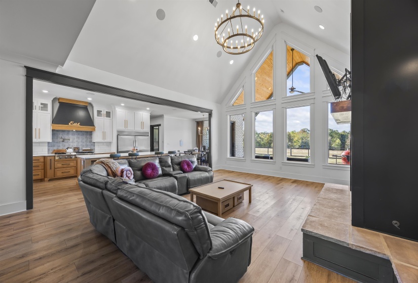 Vaulted ceiling with a chandelier, wood-finish flooring, and a stone-hearth fireplace with a dark surround