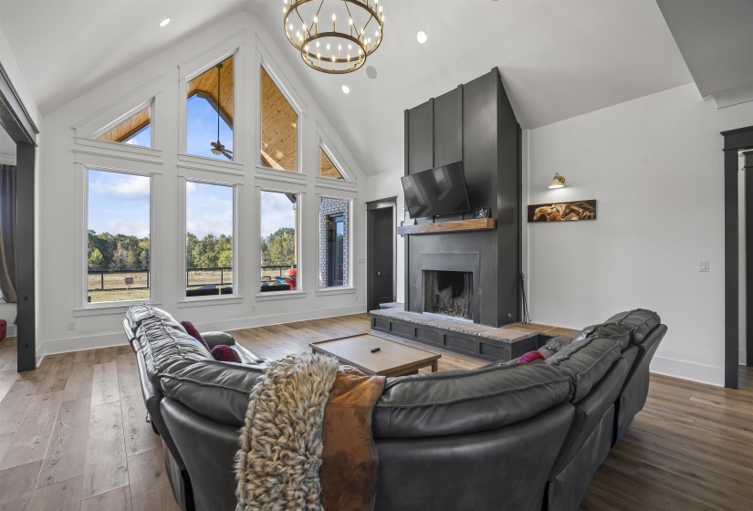 Great room featuring a vaulted ceiling with exposed wood accents, a decorative chandelier, and extensive window-walls providing abundant natural light