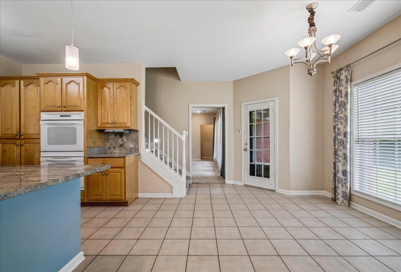 Kitchen and dining area featuring tile flooring, light wood cabinetry, a built-in oven, and a granite-look island