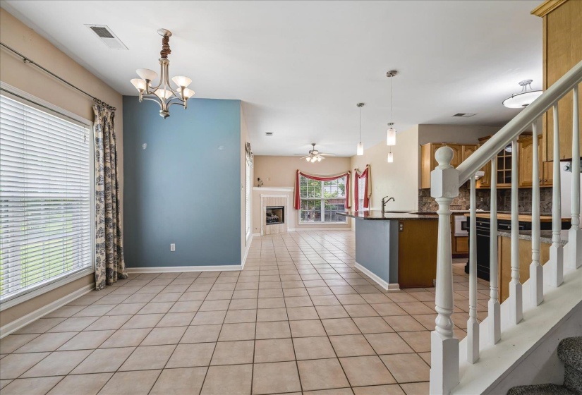 Open-concept interior featuring large tile flooring, a prominent staircase with white balusters, a kitchen island with dark countertops, and a living area with a fireplace