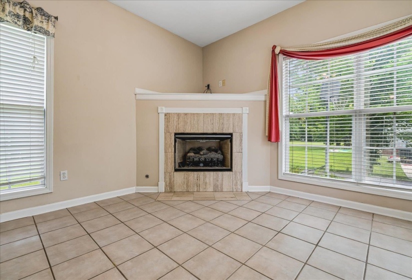 Vaulted ceiling room featuring a natural stone tile fireplace with a wooden mantel, two windows with blinds, and light-toned tile flooring
