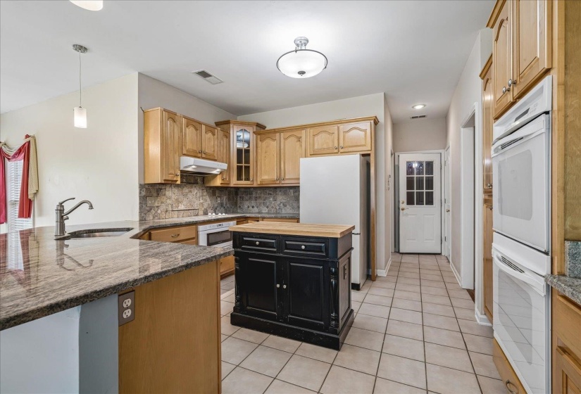 Kitchen featuring granite countertops, wood cabinetry, a central island with a wood top, tile flooring, and integrated double ovens