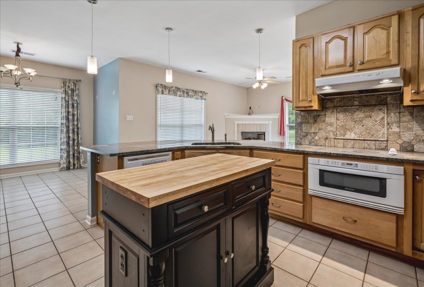 Kitchen featuring a central island with a wood-finish countertop, light wood cabinetry, stone-finish countertops, tiled flooring, and a built-in microwave