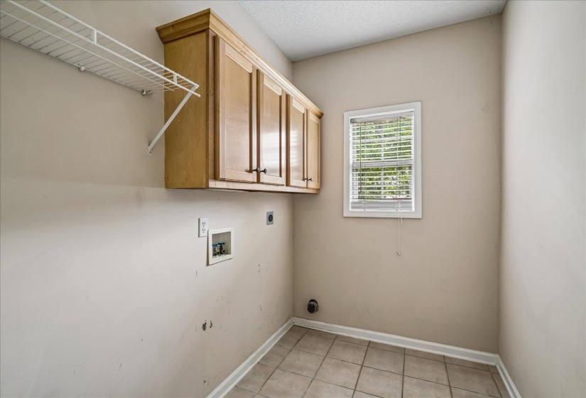Laundry area featuring wood-finish cabinetry, a white wire shelf, tile flooring, and a window with blinds