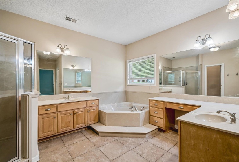 Bathroom featuring a large soaking tub, separate glass-enclosed shower, dual vanity sinks, and tile flooring