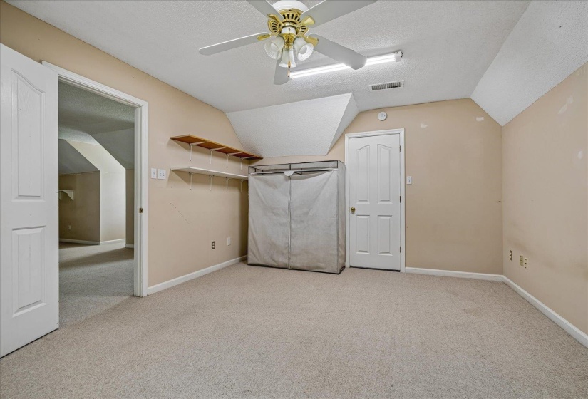Carpeted room with sloped ceilings, a ceiling fan with integrated lighting, and recessed fluorescent lighting