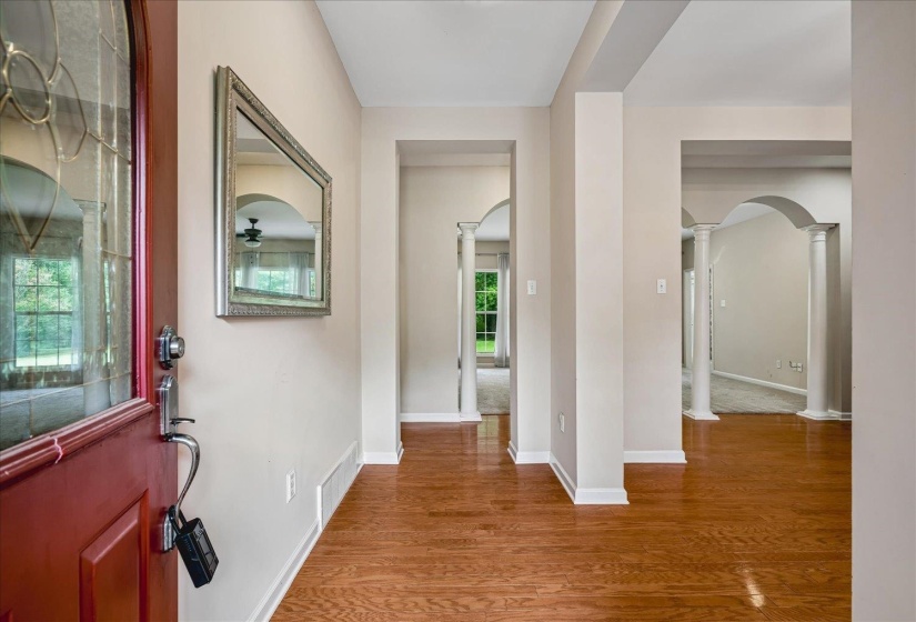 Entryway featuring wood-finish flooring, a red front door with leaded glass, and multiple arched doorways