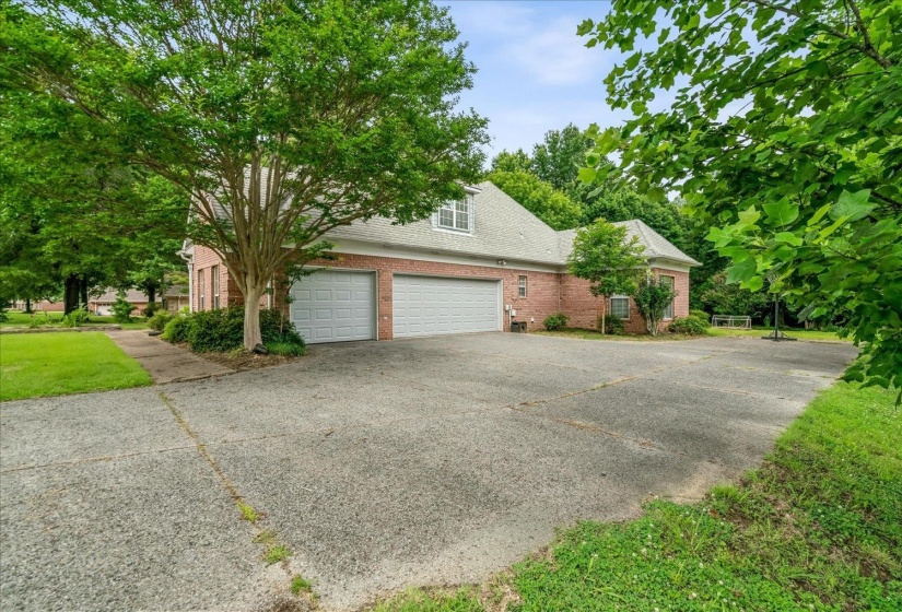 Brick exterior featuring a two-car garage with white panel doors, a gravel driveway, and surrounding mature trees