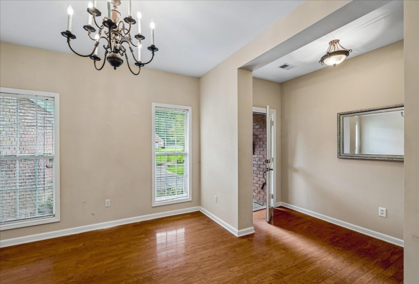 Formal dining area featuring rich wood-finish flooring, a classic chandelier, and two large windows with blinds