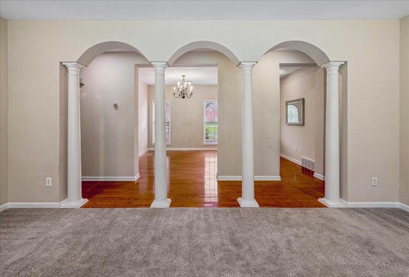 Arched entryways featuring decorative columns open to interiors with wood-finish flooring and a chandelier