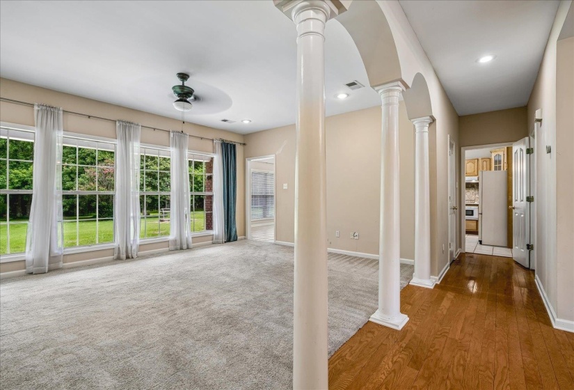 Open concept living area featuring multiple large windows overlooking a green outdoor space, a ceiling fan, recessed lighting, and a combination of carpeted and wood-finish flooring