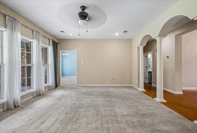 Spacious room featuring light-toned carpet flooring, multiple windows providing natural light, recessed lighting, and a ceiling fan with a circular tray ceiling detail