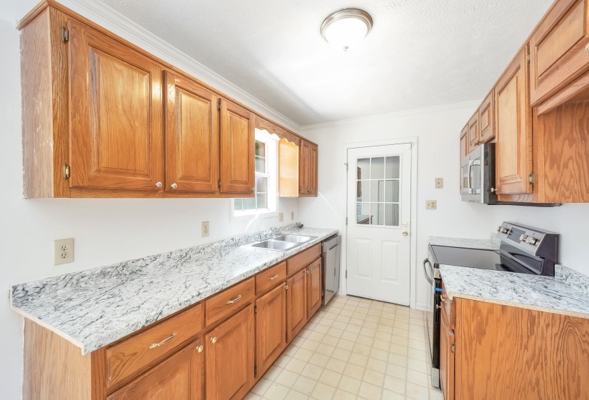 Galley kitchen featuring wood cabinetry, light-toned countertops, double basin sink, and a multi-pane glass door