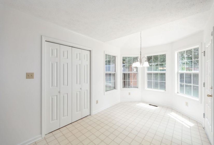 Bay window dining area with a three-light chandelier, white paneled walls, and bi-fold closet doors