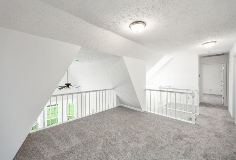 Carpeted loft area featuring white painted railings and an angled ceiling