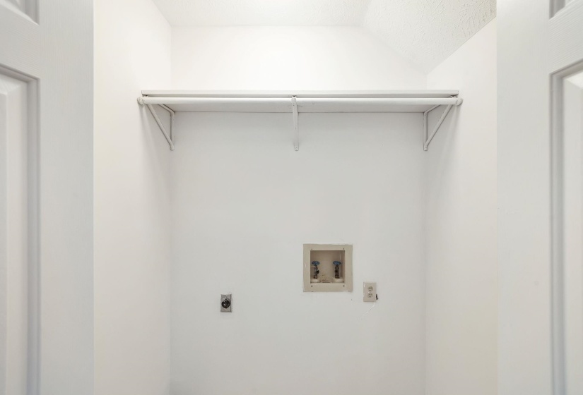 Dedicated laundry area with utility hookups and a wall-mounted storage shelf