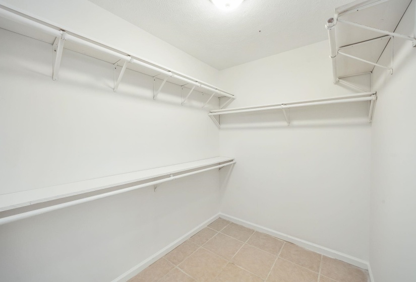 Walk-in closet featuring white wire shelving, hanging rods, and light-toned tile flooring