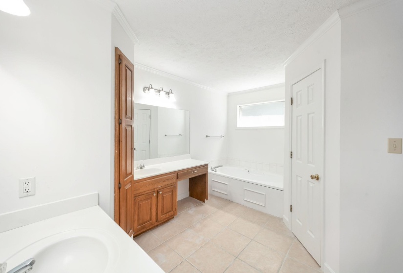 Bathroom featuring a built-in jetted tub, dual vanity with wood cabinetry, and tiled flooring