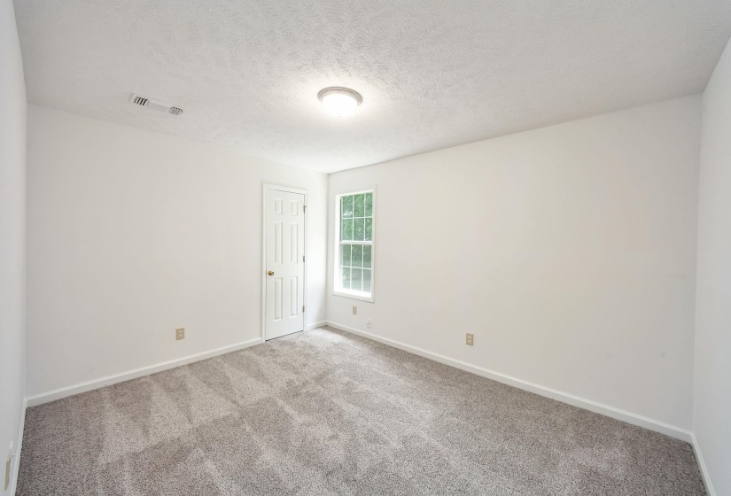 Bright room featuring light gray carpet, white walls, a white paneled door, and a white window frame with multiple panes