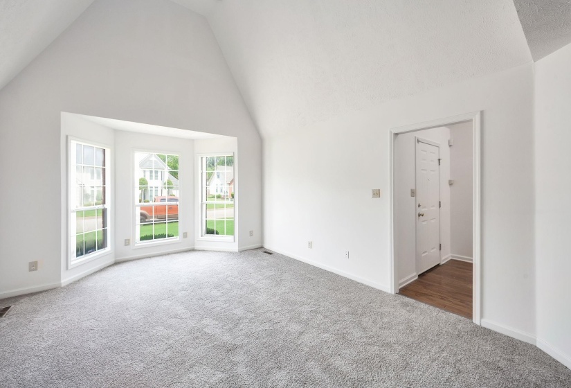 Spacious room featuring a bay window with three panes, vaulted ceiling, and light gray carpet