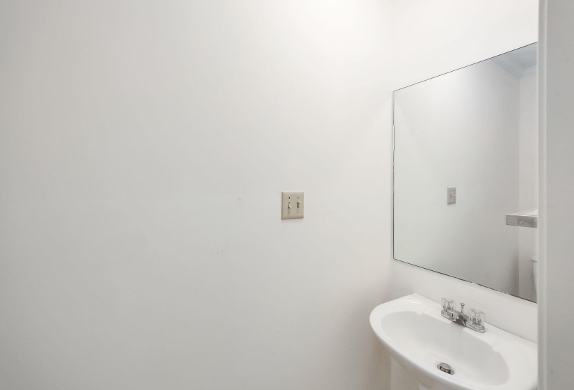 Pedestal sink with chrome faucet, large wall-mounted mirror, and neutral wall finish