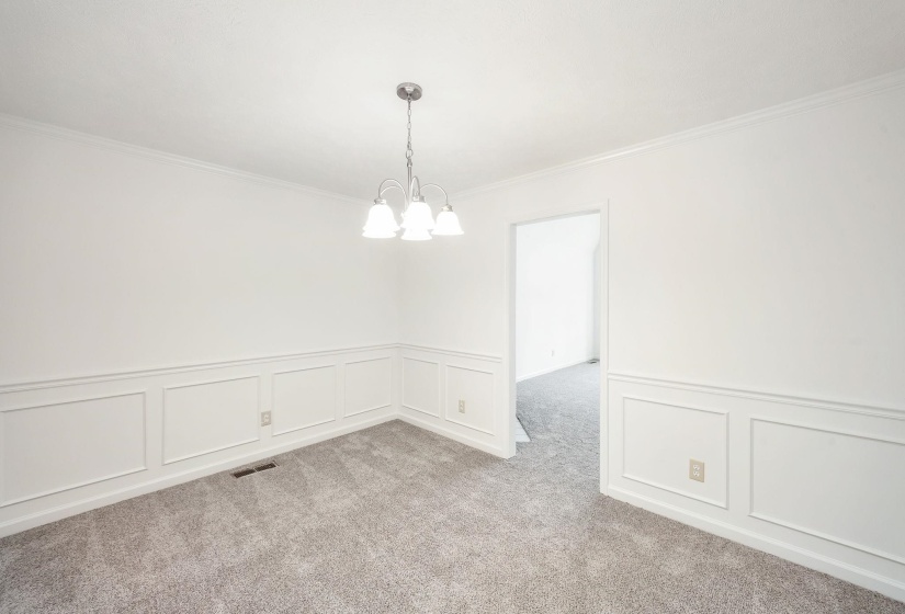 Room featuring wainscoting and crown molding, accented by a three-light chandelier