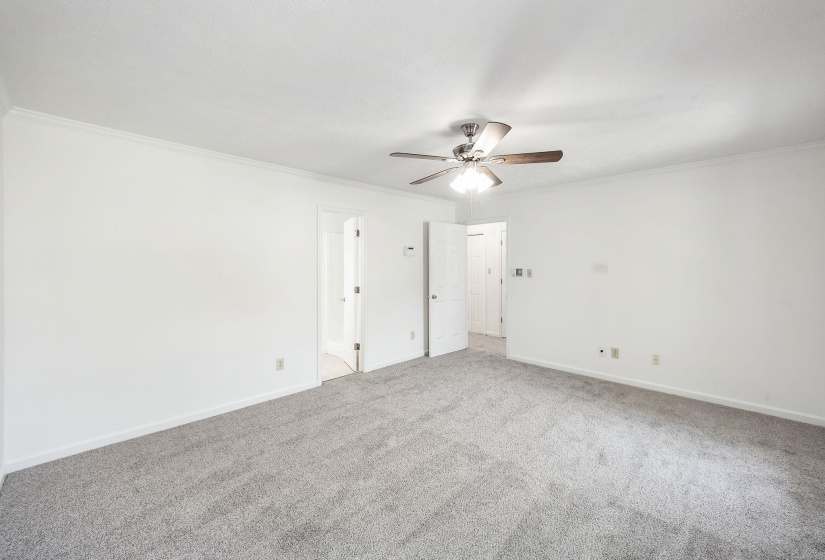 Spacious room featuring light gray carpeting, crisp white walls, and crown molding
