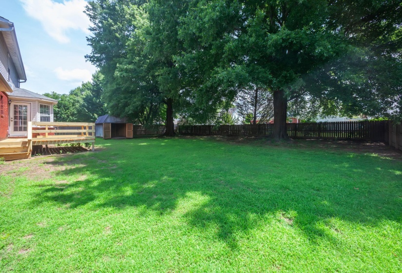 Expansive backyard featuring a large wooden deck, a storage shed, mature trees, and a privacy fence
