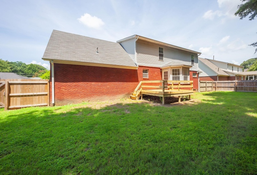 Expansive backyard featuring a wood deck, red brick exterior, light-colored siding, and a privacy fence