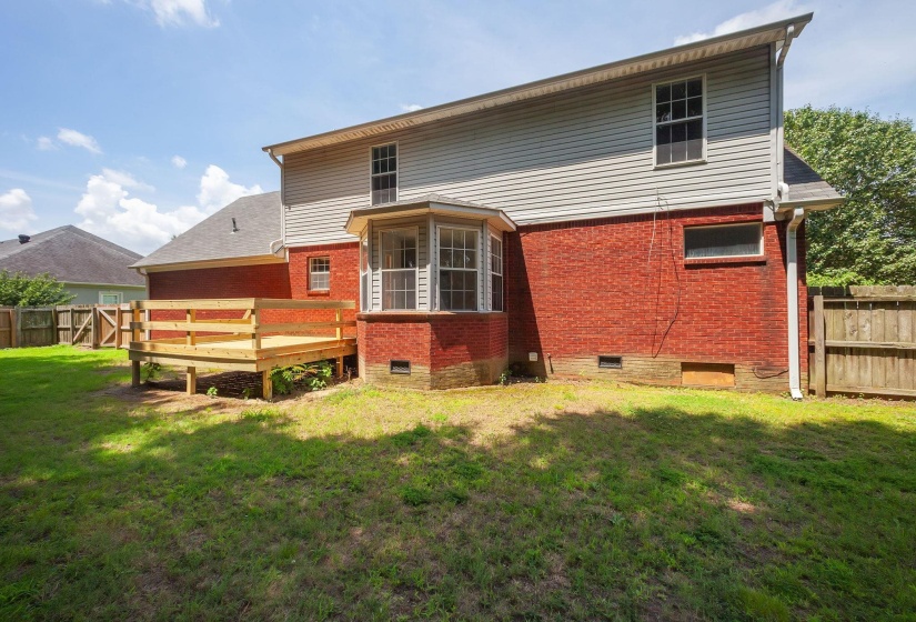 Spacious backyard featuring a new wood deck, brick foundation, bay window, and a wooden privacy fence