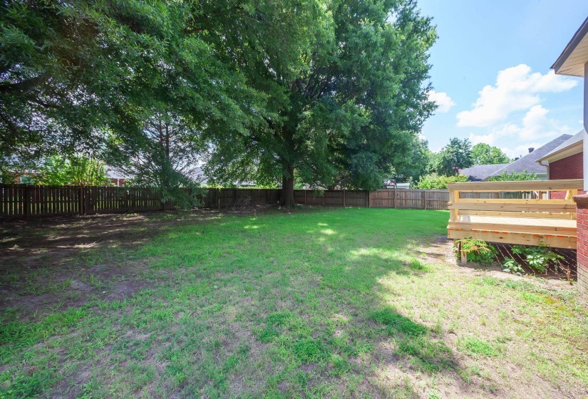Spacious backyard featuring a newly constructed wooden deck, mature shade trees, and a full privacy fence