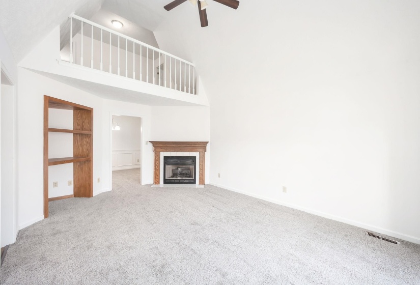Living area featuring vaulted ceilings, a built-in wood-finish bookcase, a fireplace with a wood-finish mantel, and a loft overlooking the space