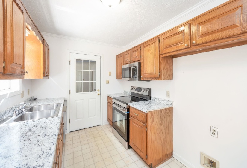 Bright kitchen featuring wood cabinetry, light-toned countertops, and a double basin stainless steel sink